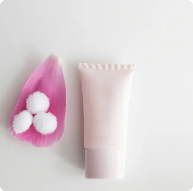 Tube de crème cosmétique accompagné de pétales de fleurs et de boules de coton, illustrant les soins beauté.