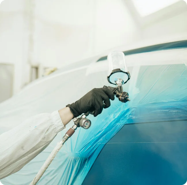 Travailleur appliquant une peinture bleue sur une carrosserie à l’aide d’un pistolet de pulvérisation.