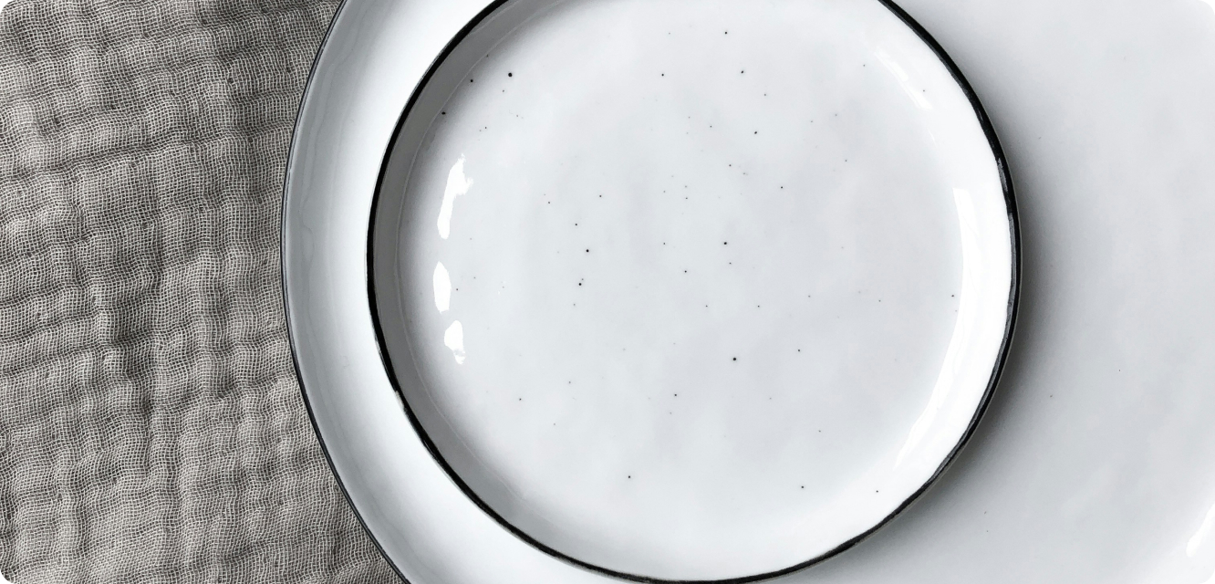 Assiette blanche avec bordure noire, posée sur une nappe texturée grise.